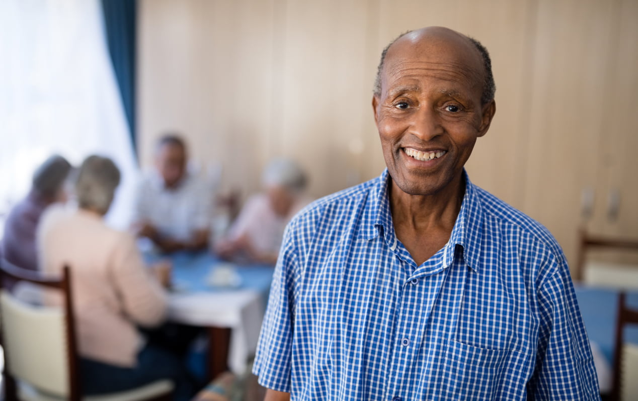 Senior man smiling in a care home with peers in the background